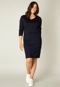 Marineblauwe shirt met lange mouwen en een v-hals, gecombineerd met een bijpassende kokerrok en witte sneakers. Gladde stof met een aansluitende pasvorm.