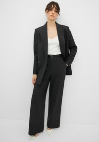 Completo con righe nere composto da blazer a doppio petto e pantaloni a gamba larga. Indossato sopra una maglietta bianca, completato da una cintura nera e scarpe a punta.