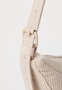 Borsa in corduroy beige chiaro con superficie testurizzata, dotata di una larga tracolla fissata da una fibbia in plastica beige.