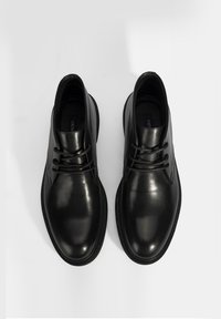 Chaussures en cuir noir avec une finition lisse et brillante, dotées de lacets ronds et de subtils accents de couture sur les côtés. Design et forme classique.