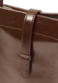 Brązowa torebka z syntetycznej skóry o gładkiej fakturze, z płaskim paskiem, zapięciem na nap i widocznymi detalami ściegów.