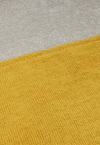 Rechteckiger Teppich mit einem strukturierten gelben Abschnitt neben einem hellgrauen Bereich, beide mit einem gewebten Muster und einer weichen, plüschigen Oberfläche.