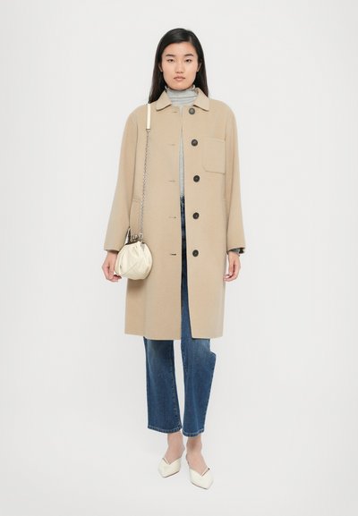 Beige coat with a collar, front buttons, and side pocket, paired with gray turtleneck and blue jeans. Model holds a cream pouch bag.