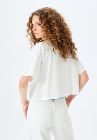 Gekürztes weißes T-Shirt aus weichem Stoff mit kurzen Ärmeln, kombiniert mit weißen Hosen mit Taschen hinten und einem hellblauen Bund.