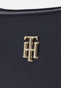 Borsa in pelle nera texturizzata con un logo metallico dorato prominente con lettere intrecciate, che mette in evidenza il design elegante della borsa.