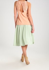 Top senza maniche color pesca con dettagli in pizzo sul retro, abbinato a una gonna fluida verde menta. Scarpe con tacchi alti beige completano l'outfit.