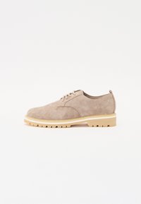 Beige suede shoe with a rounded toe, lace-up design, and a cream-colored, rugged rubber sole. Minimalist style with no prominent features.