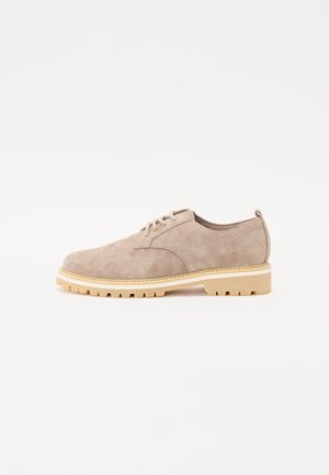 Beige suede shoe with a rounded toe, lace-up design, and a cream-colored, rugged rubber sole. Minimalist style with no prominent features.