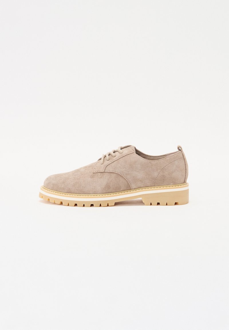 Beige suede shoe with a rounded toe, lace-up design, and a cream-colored, rugged rubber sole. Minimalist style with no prominent features.