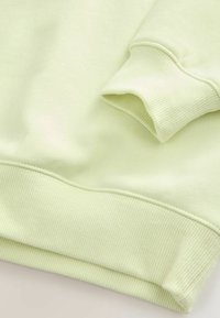 Poignets et bord inférieur de sweat-shirt vert clair avec texture côtelée et coutures visibles sur un tissu doux.