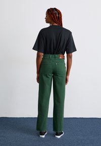 Green wide-leg jeans with a high waist, featuring two back pockets and a leather patch, paired with a loose black t-shirt.