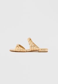 Χρυσά σανδάλια με επίπεδη σόλα και στριφτές λουρίδες, με ορθογώνιο σχέδιο στη μύτη. Το επάνω μέρος έχει ελαφρώς γυαλιστερή υφή, με επίπεδη σόλα.