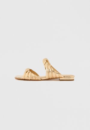 Sandales plates dorées avec des brides torsadées et un design à bout rectangulaire. La tige présente une texture légèrement brillante, avec une semelle plate.
