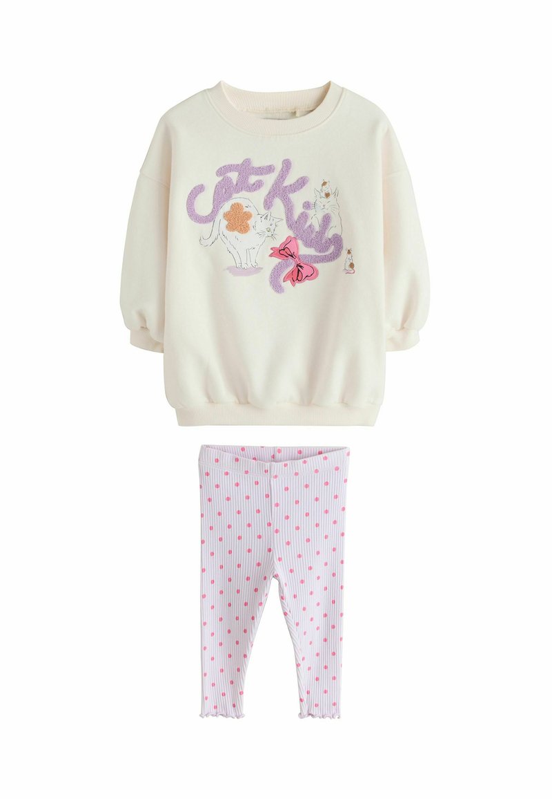 Felpa color crema con illustrazioni di gatti e dettagli viola, abbinata a leggings rosa a pois. Tessuto morbido, polsini a coste e orlo arricciato.