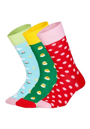 Tre farverige sokker med påsketema: blå med kaniner og æg, grøn med gule kyllinger og rød med hvide polkapletter.