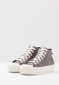 Höga sneakers i metallisk lila tyg med vita snören och solida vita gummisulor. Har en tre-stripes design på sidan.