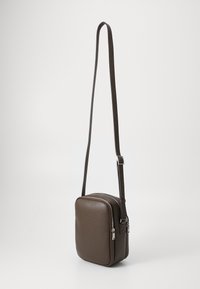 Brun skinn crossover bag med rektangulær form, sølv glidelås og justerbar stropp. Teksturet overflate med en glatt finish.