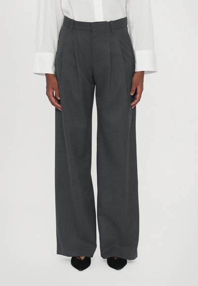 Pantalones de tiro alto en gris con pliegues frontales, cinturilla ajustada y textura suave; combinados con zapatos de tacón negros de punta afilada y una camisa blanca.