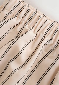 Tela beige con rayas negras verticales y una cintura elástica, mostrando pliegues recogidos y detalles de costura.