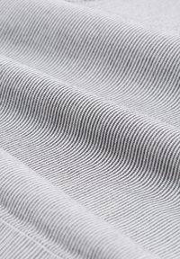 Tissu texturé en blanc avec de fines rayures noires ondulées, créant un motif rythmique. Le matériau semble léger et lisse au toucher.