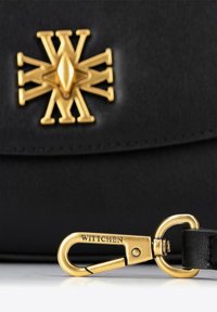 Borsa in pelle nera con un prominente emblema dorato e una chiusura dorata con "WITTCHEN" inciso, che mette in risalto il suo hardware e la sua texture.