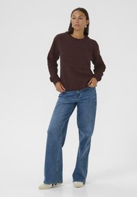 Sweat-shirt bordeaux avec un design de numéro embossé sur le devant, associé à un jean large bleu clair et des baskets beiges. Matière lisse et coupe décontractée.