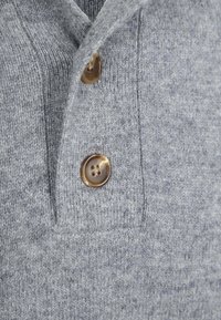 Nahaufnahme eines grauen Strickstoffs mit zwei in einer vertikalen Blende angenähten Schildpattknöpfen.