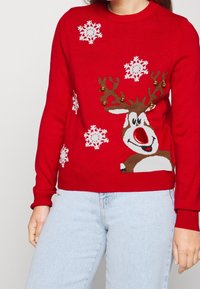 Maglione rosso a maglia con una grafica di renna con corna e un naso rosso, accentuato da fiocchi di neve bianchi e decorazioni dorate.