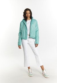 Giacca a vento color acquamarina con design trapuntato, polsini elasticizzati e colletto alto. Indossata sopra una maglietta bianca a coste e jeans bianchi strappati.
