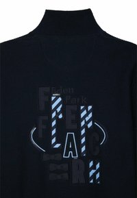 Pull marin avec col montant, présentant une lettrage texturé et des rayures en bleu et bleu clair. Comprend des accents de nœud papillon dans le design.