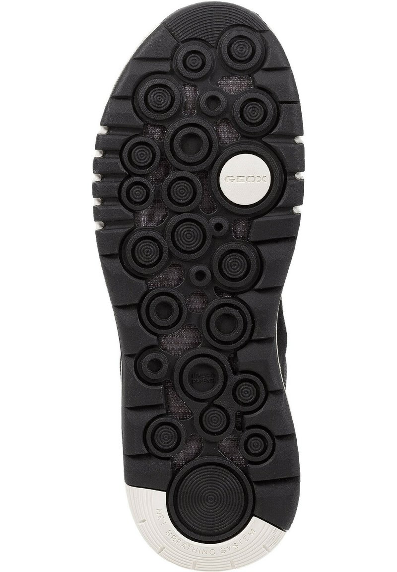 Semelle de chaussure en caoutchouc noir avec des motifs circulaires et des accents texturés, présentant un détail de marque blanc et un design d'aération circulaire.