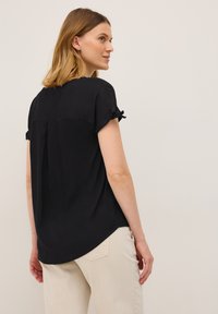 Sort kortærmet bluse med opsmøg på ærmerne, en rygplisse og en buet kant. Glat stof, letvægts og afslappet design.