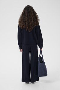 Navyblå oversized genser med løse ermer, kombinert med marineblå bukser med vide ben. En myk, teksturert grå totebag holdes i den ene hånden.