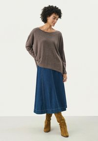 Bruine gebreide trui met een wijd decolleté, gecombineerd met een lange spijkerrok. Hoge gele suède laarzen maken de outfit compleet.