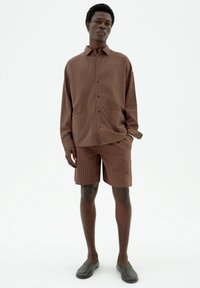 Brown striped shirt and shorts set made of lightweight material, featuring a relaxed fit and button closure, complemented by flat shoes.