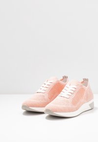 Světle růžové síťované tenisky s bílými tkaničkami, texturovaným povrchem a polstrovanou podrážkou; mají hladký zaoblený špičku a vycpaný límec.
