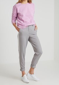 Ljusrosa sweatshirt med rund hals, tillsammans med grå tapered byxor med sidostreck och uppvikta ärmslut. Vita sneakers fulländar looken.