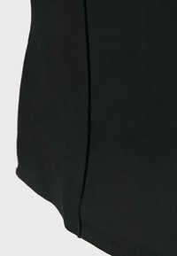 Gros plan sur un vêtement en tissu noir montrant une couture verticale centrale avec des détails de couture propres et lisses.