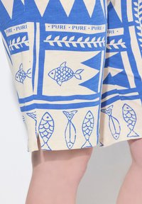 Pantaloni corti in cotone con pesci blu e motivi geometrici su uno sfondo crema, caratterizzati da spacchi all'orlo per un tocco di classe.