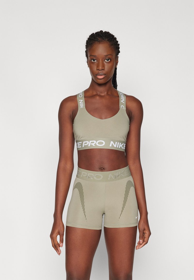 Sostén deportivo Nike Pro en verde oliva y pantalones cortos, con una textura suave, un logo blanco en contraste y un patrón sutil en los pantalones.