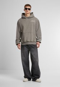 Grey hoodie with a large front pocket and ribbed hem, paired with loose black denim pants featuring a textured pattern. White sneakers.
