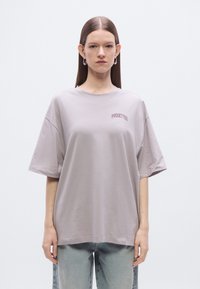 Light gray oversized t-shirt with short sleeves. Features embroidered text "PIRUETTES" in dark red. Soft cotton blend fabric.