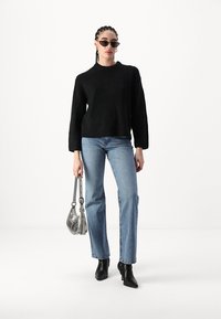 Juodas megztinis su plačiomis rankovėmis, derinamas su šviesiai mėlynomis tiesiomis kelnėmis. Papuoštas sidabrine rankine ir juodais aukštakulniais batais.