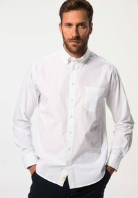 Weißes Button-Down-Hemd mit einer Brusttasche, langen Ärmeln, klassischem Kragen und subtiler Textur. Getragen mit dunkelfarbigen Hosen.