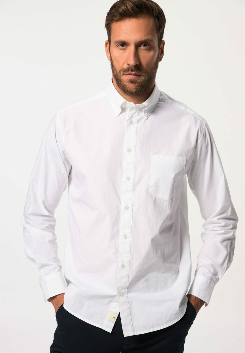 Weißes Button-Down-Hemd mit einer Brusttasche, langen Ärmeln, klassischem Kragen und subtiler Textur. Getragen mit dunkelfarbigen Hosen.