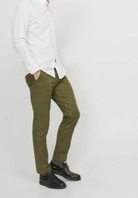 Olive green chinos with a slim fit and flat front, paired with a white button-up shirt and black leather shoes. Smooth fabric texture.