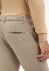Pantalons beige ajustés en tissu texturé, dotés de poches latérales et d'une seule poche arrière au design lisse et plat.