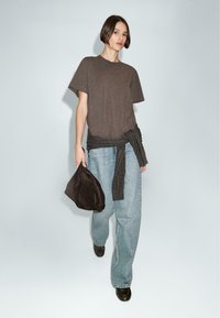 Brown short-sleeve t-shirt, loose blue jeans, and a dark brown handbag. The outfit features a tied sweater at the waist and black shoes.