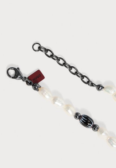 Chaîne en métal noire avec des perles blanches et une perle décorative noire, avec un fermoir mousqueton et une petite étiquette rouge portant la mention Hugo.