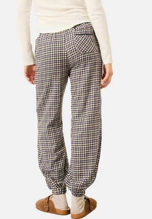 Checked-pattern trousers in navy, cream, and burgundy, featuring elastic cuffs, side pockets, and a back pocket detail. Worn with slip-on shoes.